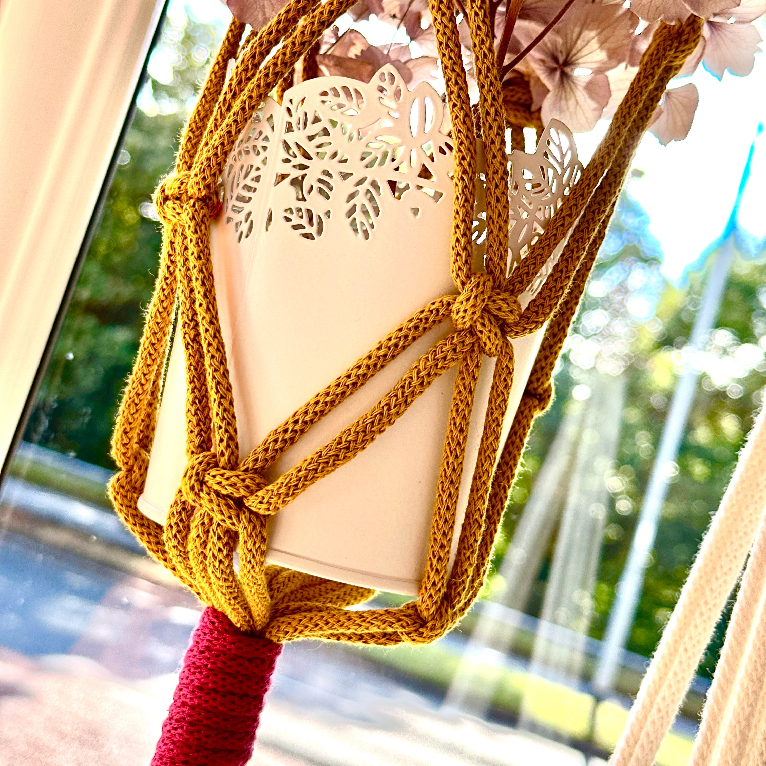 Decorative lantern with knotted yellow rope and red tassel against a blurred natural background