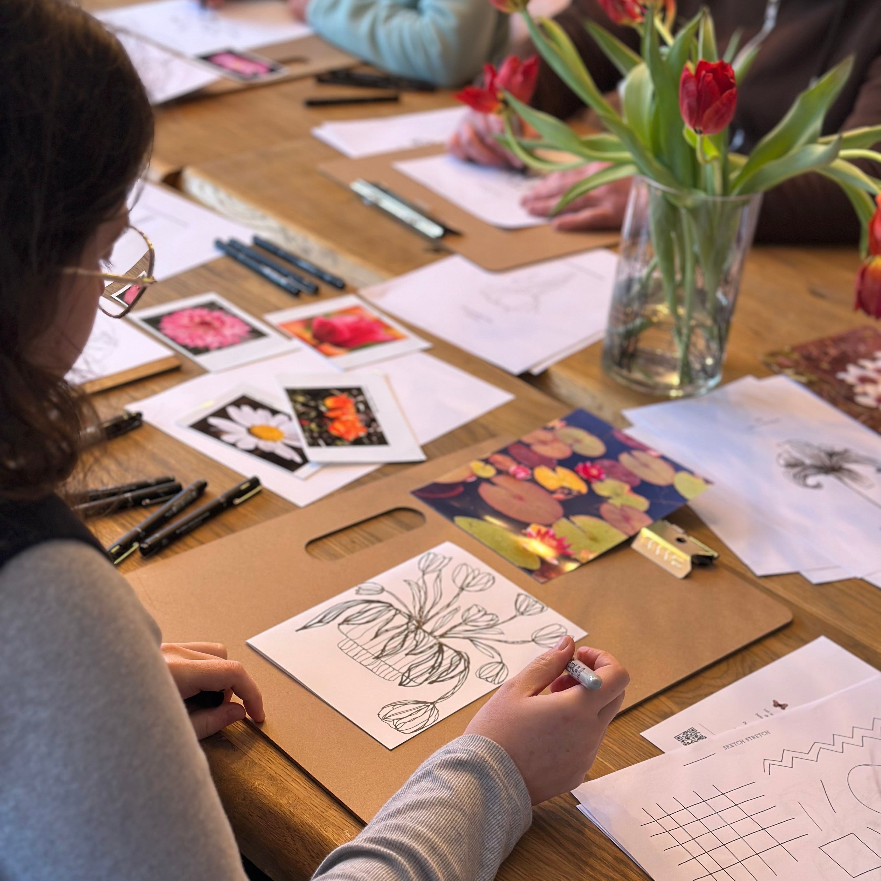 People working on art projects at a table with flowers and stationery.
