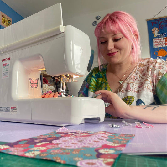 Person with pink hair using a sewing machine in a home setting
