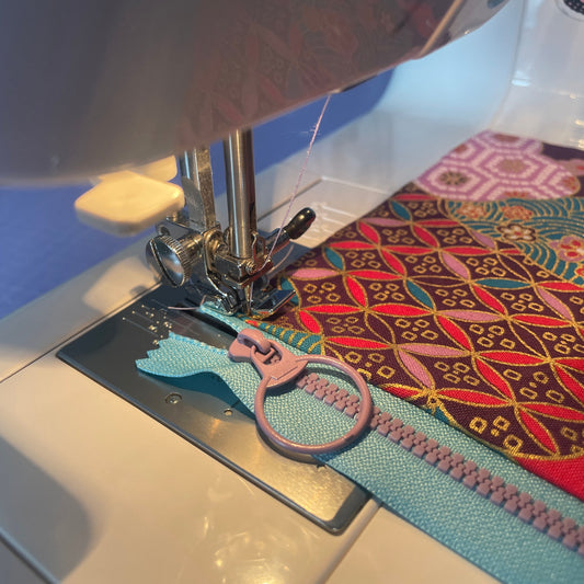 Sewing machine stitching a colorful fabric with a zipper attachment.