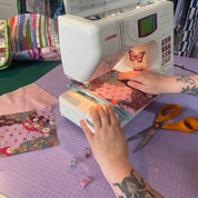 Person using a Janome sewing machine on a quilt with colorful fabric pieces.