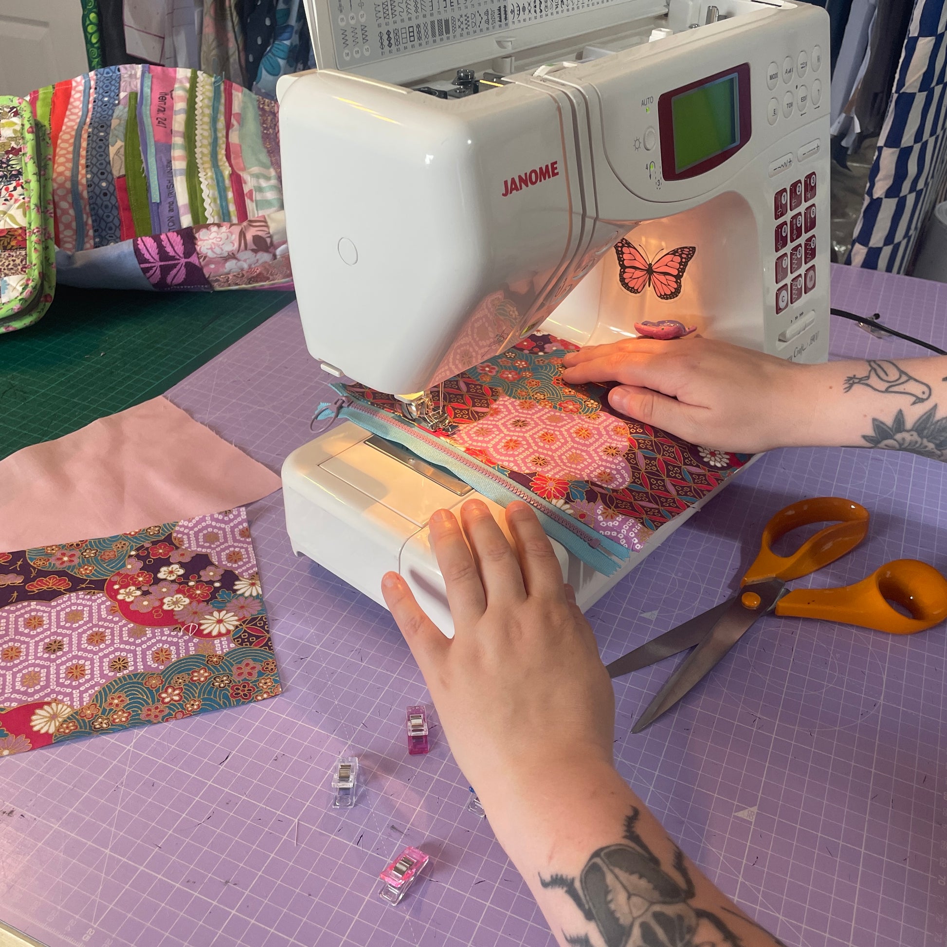 Person using a Janome sewing machine on a quilt with colorful fabric pieces.