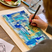 Person painting a blue and yellow abstract artwork on a wooden surface.