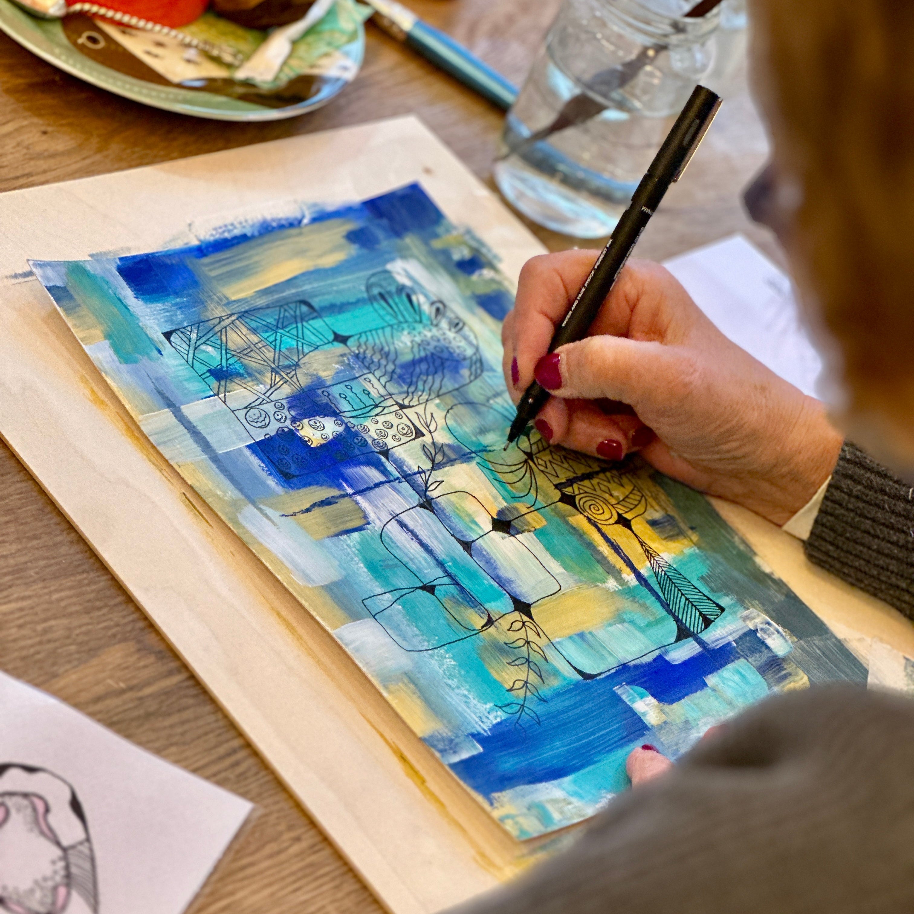 Person painting a blue and yellow abstract artwork on a wooden surface.