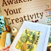 Hand holding a card with artistic design in front of a 'Awaken Your Creativity' sign.