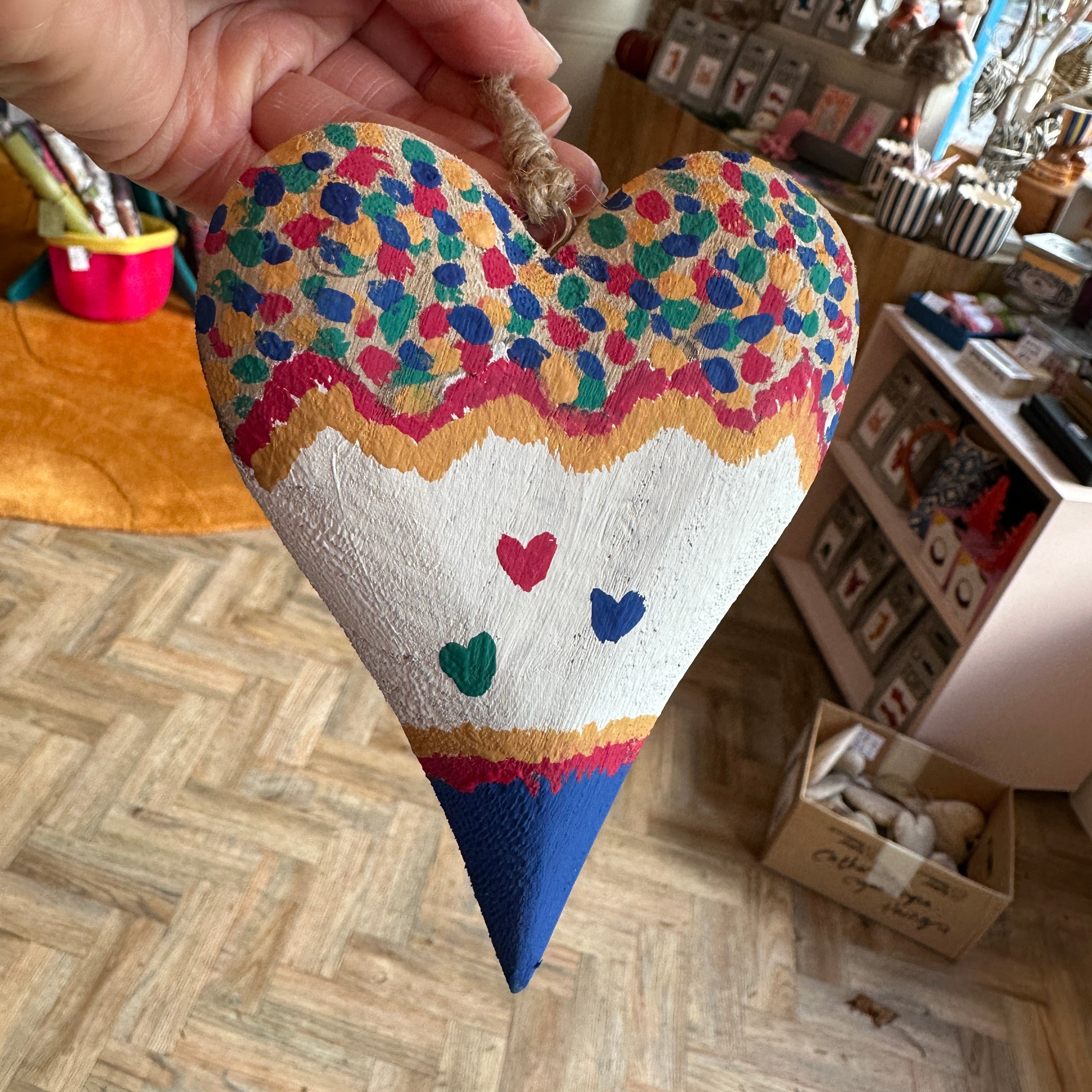 Heart-shaped pillow with colorful patterns held by a hand on a wooden floor.