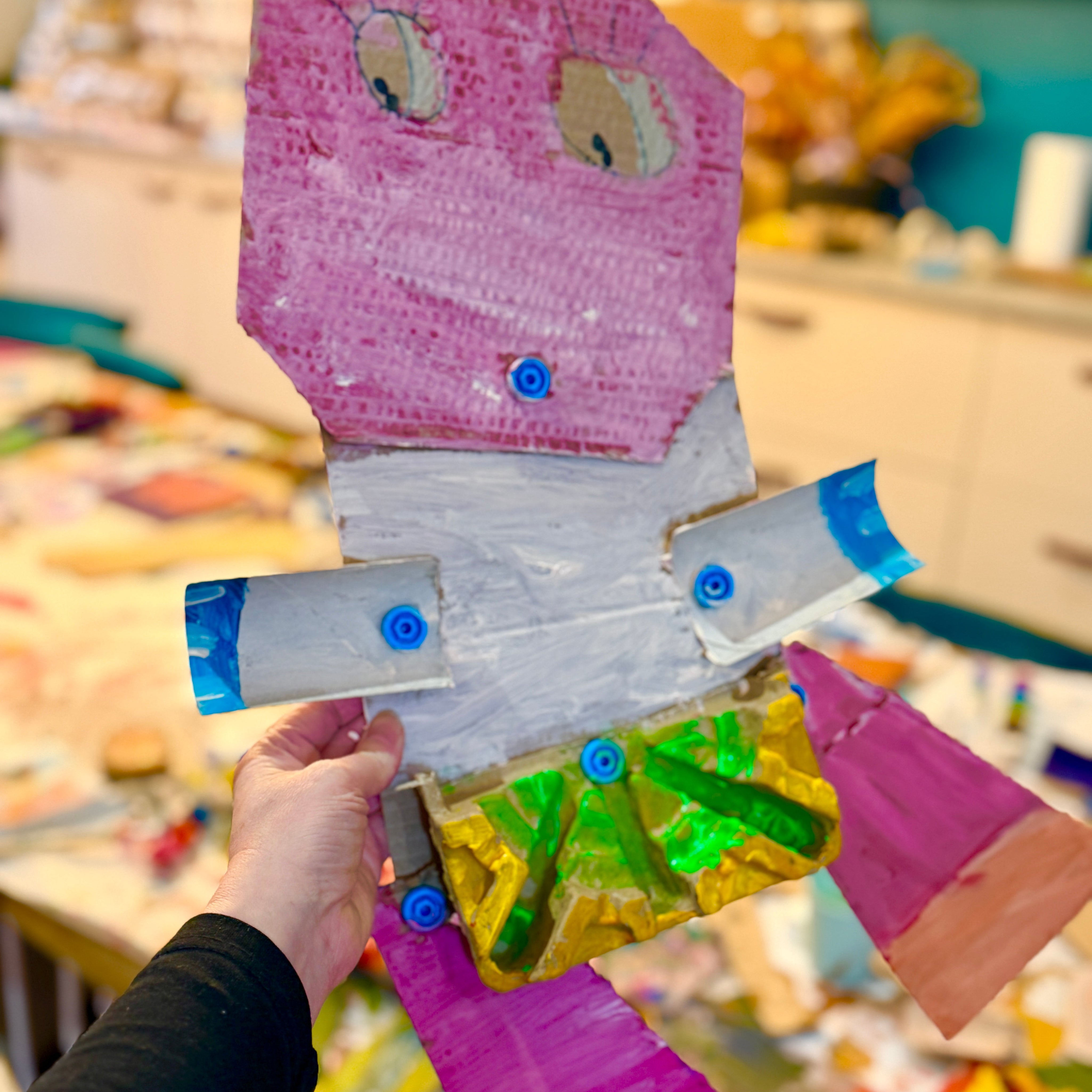 Handmade paper craft airplane with colorful design held by a person in an indoor setting.