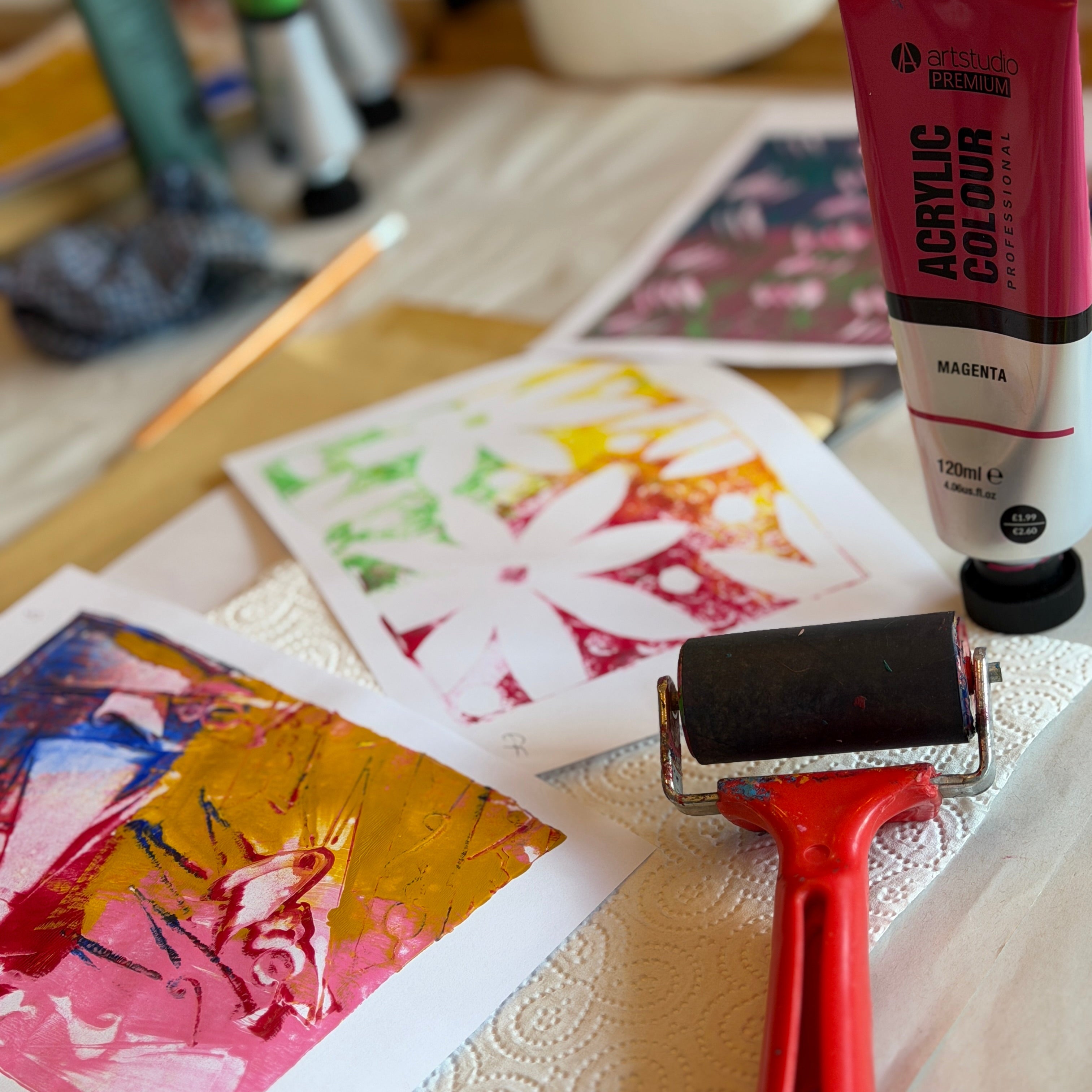 Acrylic paint tube, roller, and colorful artworks on a table