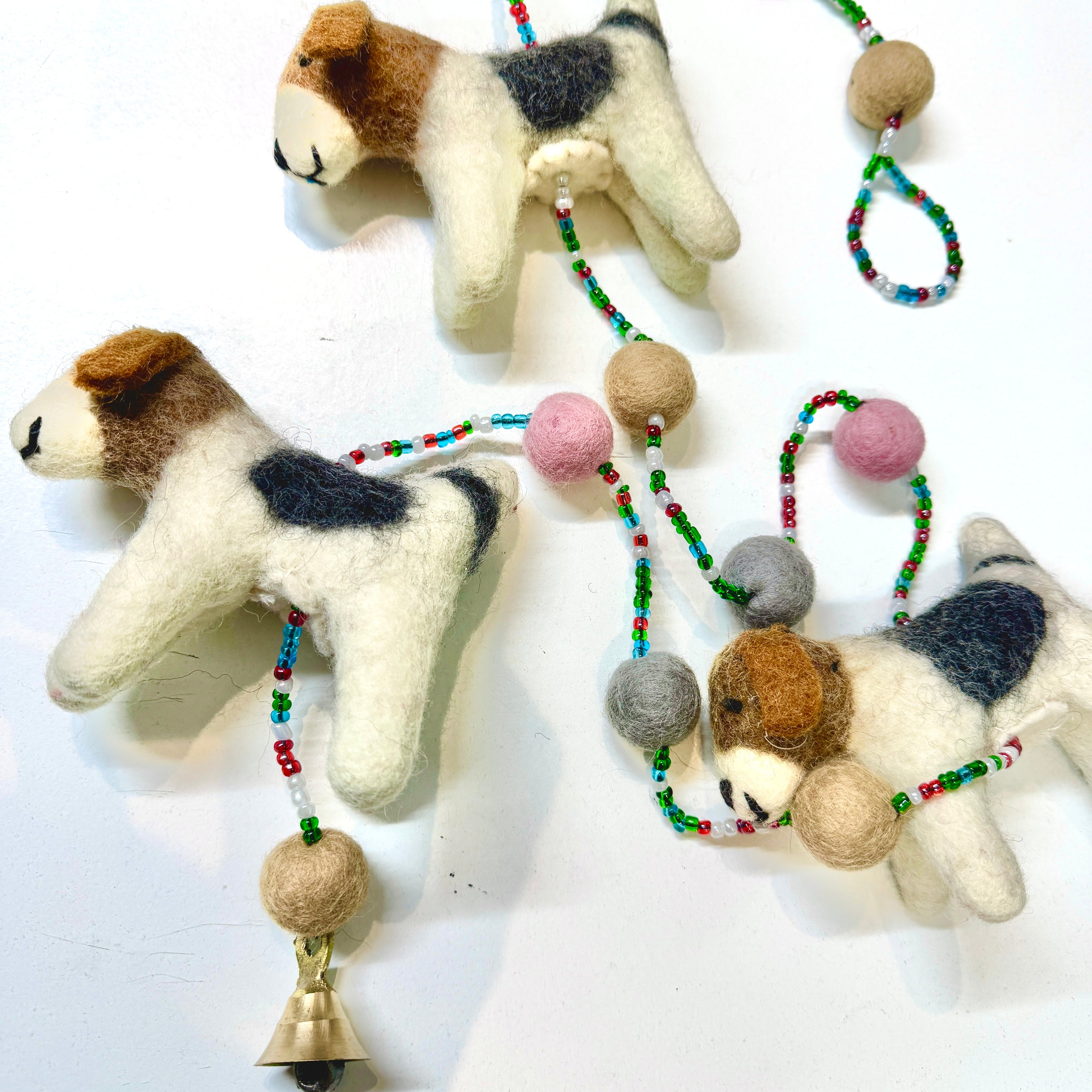 Three felted dog toys with bead and bell decorations on a white background