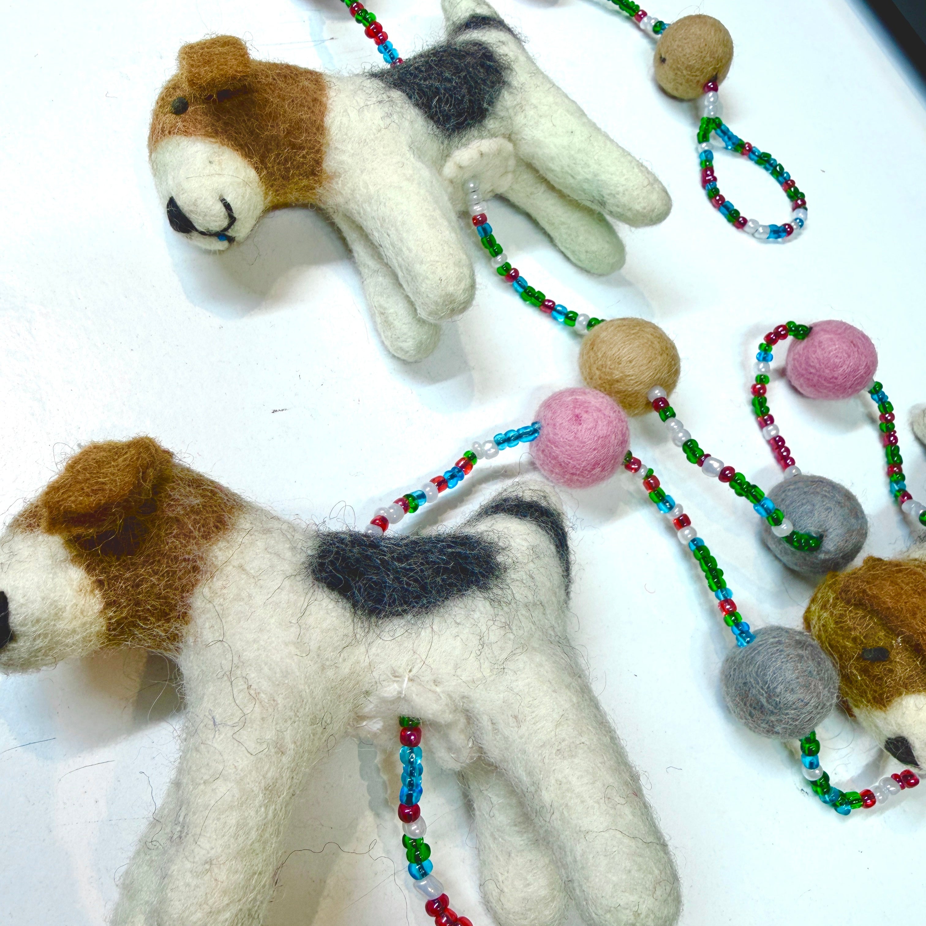 Two felted dog toys with a string of beads on a white surface
