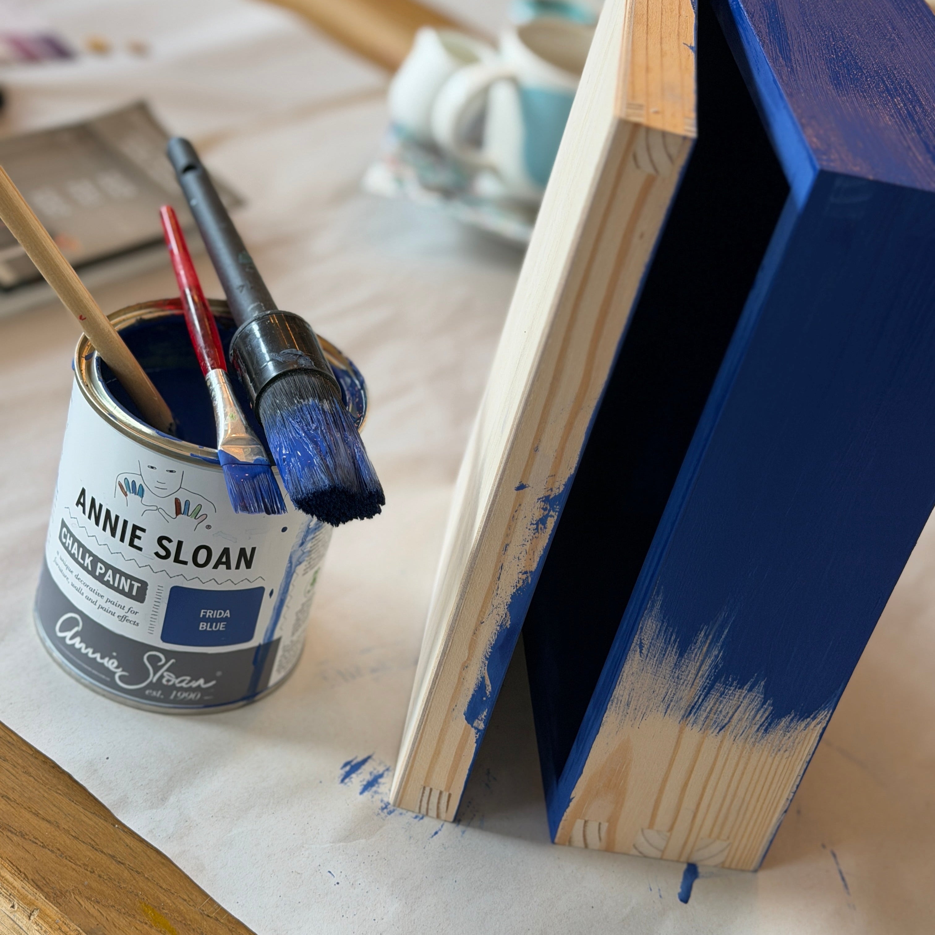 Blue-painted wooden book with Annie Sloan paint can and brushes on a table.