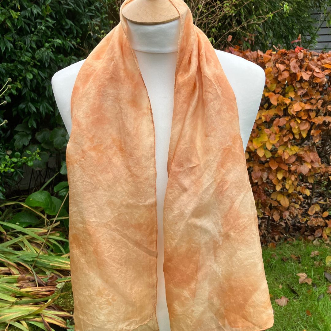 Mannequin wearing a peach-colored scarf with a garden background