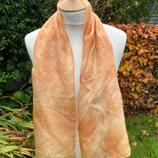 Mannequin wearing a peach-colored scarf with a garden background