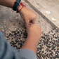 Person wearing a textured sleeve and a watch with a red string, standing on a concrete surface.