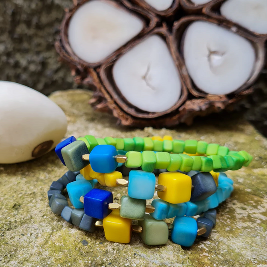 Stack of colorful beaded bracelets on a textured surface with candles in the background
