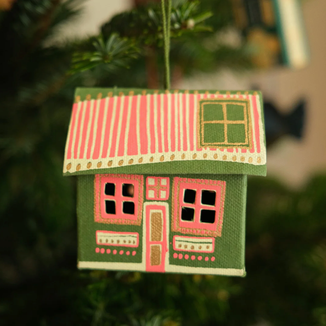 Decorative house ornament with a red roof hanging on a Christmas tree.
