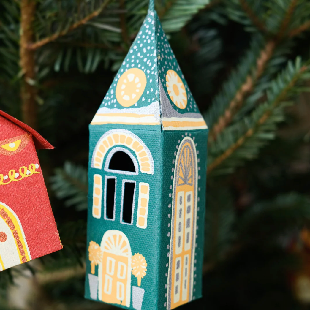 Decorative paper house ornament with architectural details on a Christmas tree.