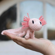 Pink crochet axolotl toy held in a hand with a blurred background