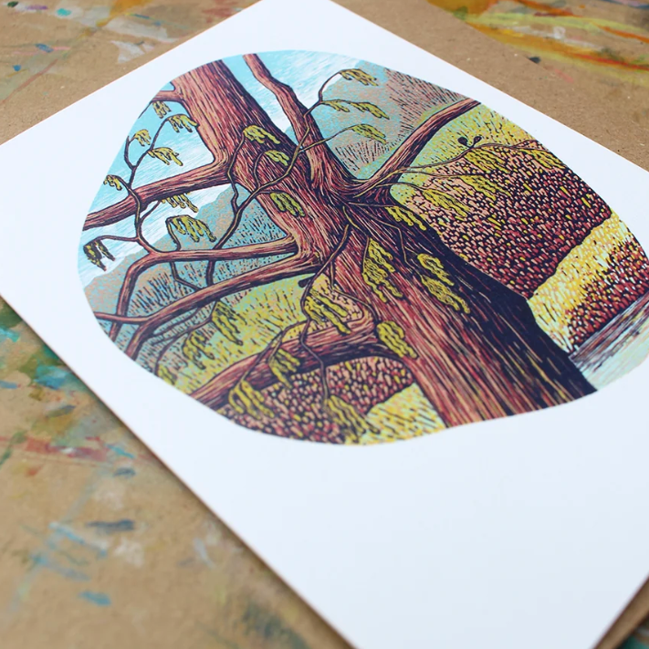 A square white art print featuring a colorful illustration of a tree trunk and branches with green and yellow foliage, shown on a painted brown paper surface. Two small thumbnails at the bottom show close-ups of the print and the full layout.