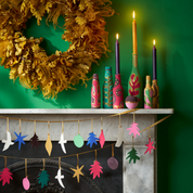 A screenshot of a web browser showing an article about making fun and bright mason jar candles, with a featured image of a decorated mantel featuring colorful mason jars, a gold wreath, and hanging star ornaments.