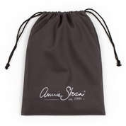 A screenshot of an e-commerce product page for the Annie Sloan Apron, showing a dark brown apron with a white script logo and a matching dark brown drawstring bag on the right. The left side contains product details, pricing, and a pink 'Kiarna available at checkout.