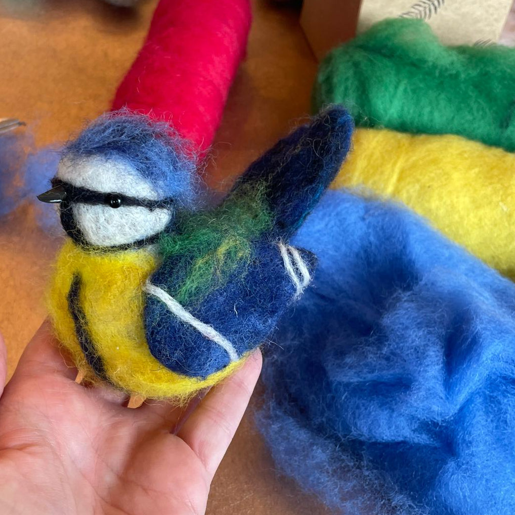Hand holding a felted bird toy with colorful fibers on a wooden surface