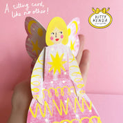 Card shaped like a butterfly woman with pink and yellow design, held against a pink background.