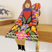 Colorful butterfly-shaped figurine with a heart design on a wooden surface, branded 'Butterfly Women by Kitty Kenda'.