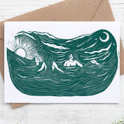 Greeting card with ocean design featuring people and a brown envelope on a white wooden surface.