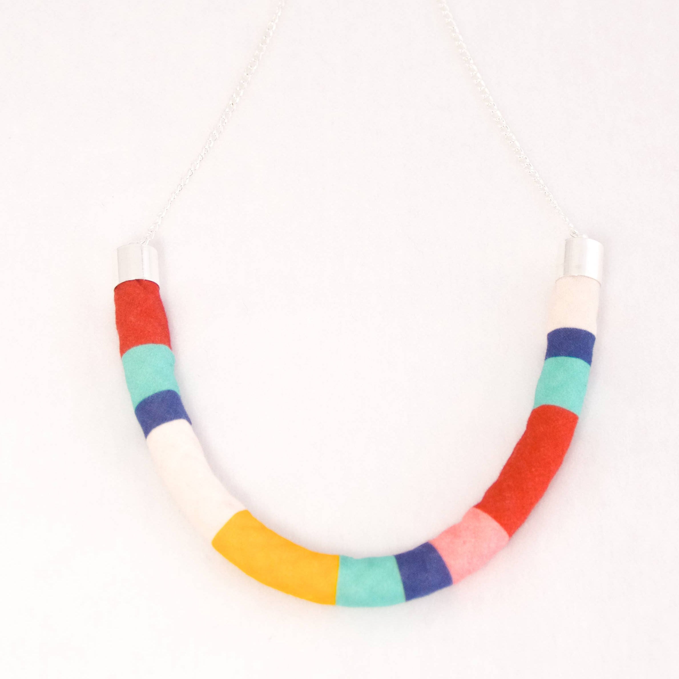 A handmade U-shaped necklace made of colorful fabric-covered segments in red, white, blue, yellow, pink, and mint green, hanging from a silver chain against a plain white background.