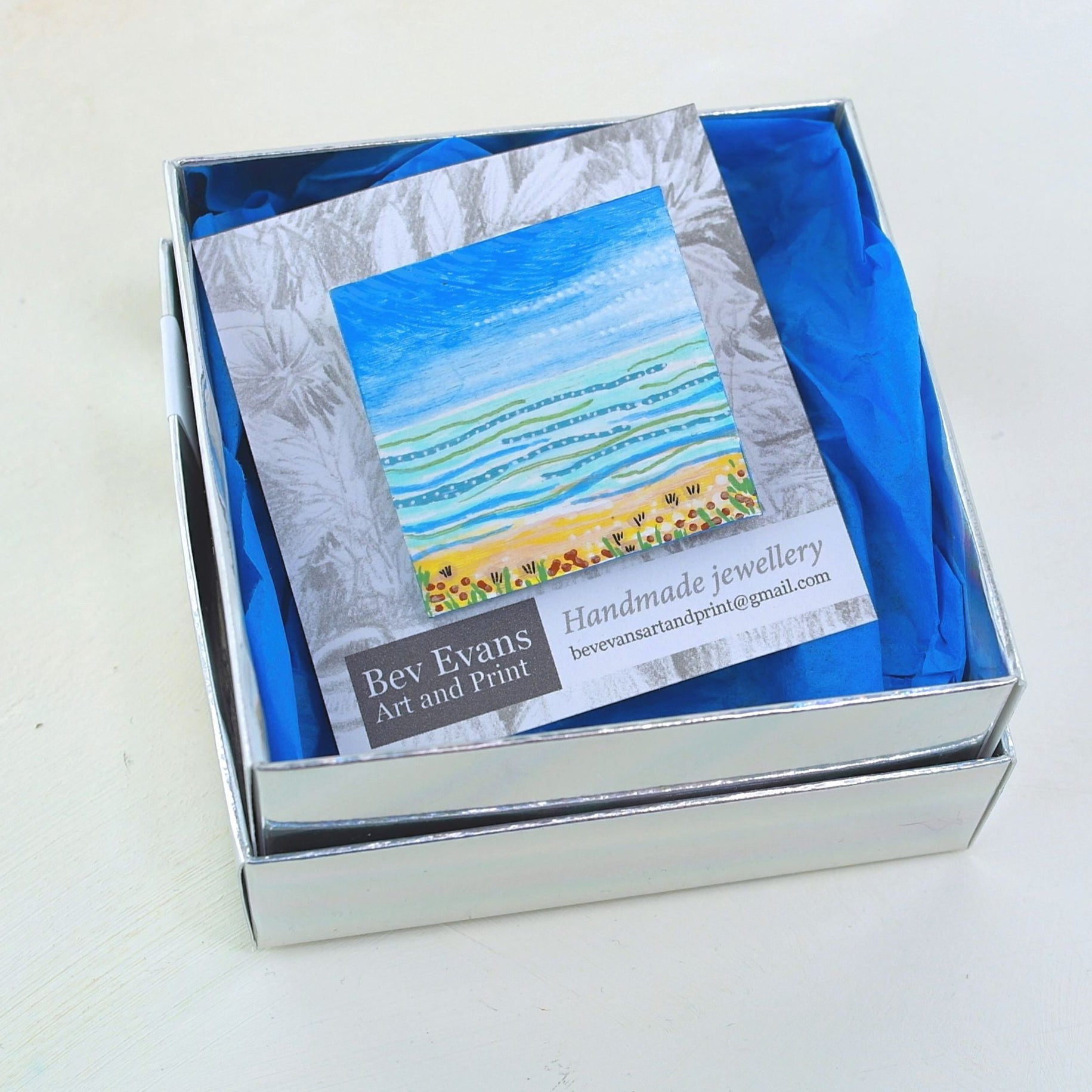 Box containing a card with a watercolor design and text on a white background