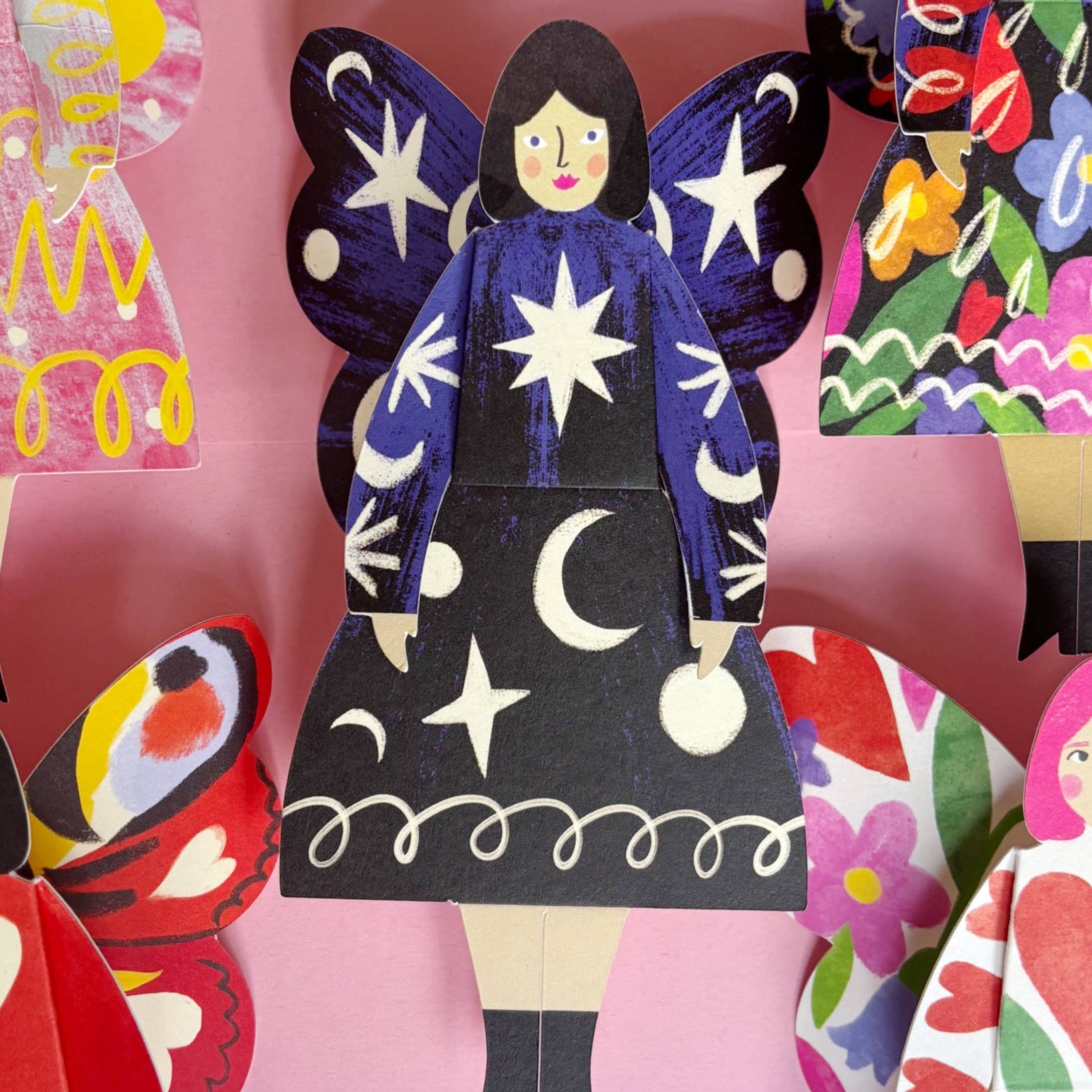 Colorful paper dolls with a prominent butterfly-themed doll on a pink background, featuring the Kitty Kenda brand.