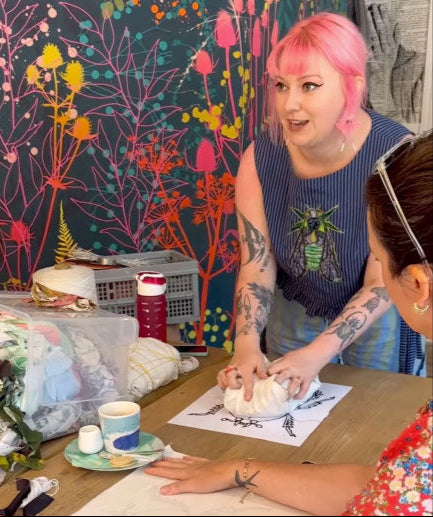 Two people at a table with various items, including a colorful wall in the background.
