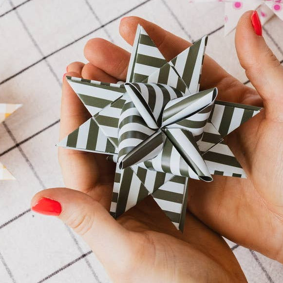 Hand holding a black and white striped paper star with more stars in the background on a checkered surface.