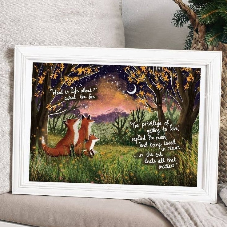 Framed artwork of two foxes under a tree with a quote, placed on a surface.