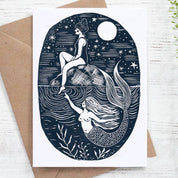 Greeting card with mermaid design on a white wooden surface with a brown envelope.