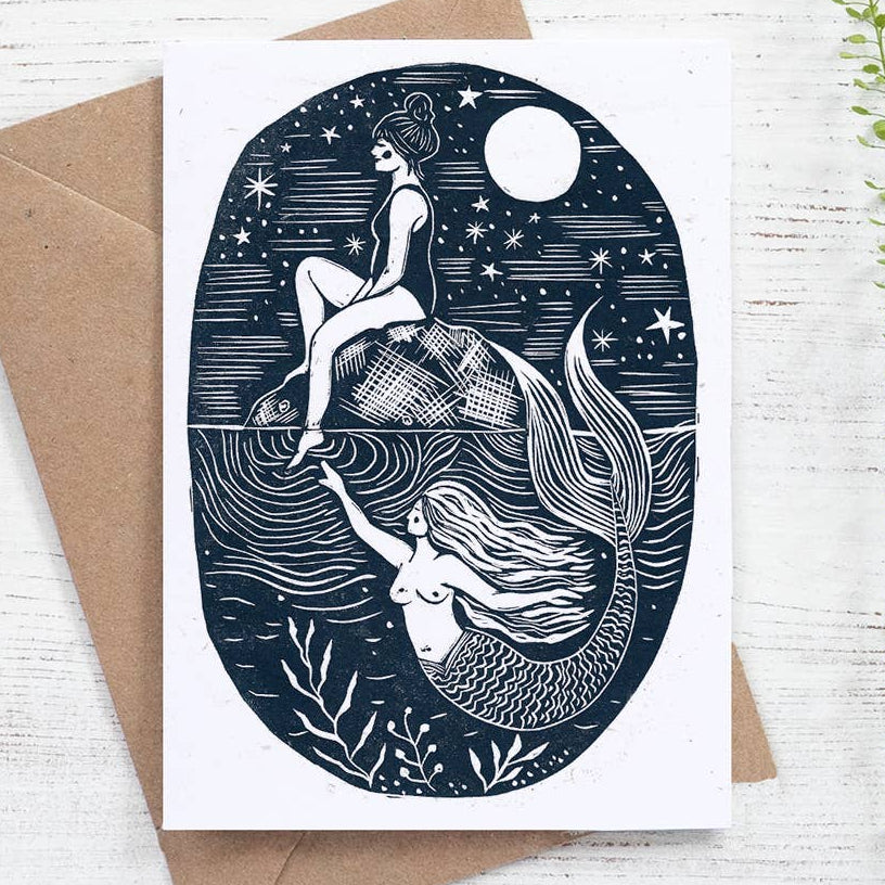 Greeting card with mermaid design on a white wooden surface with a brown envelope.