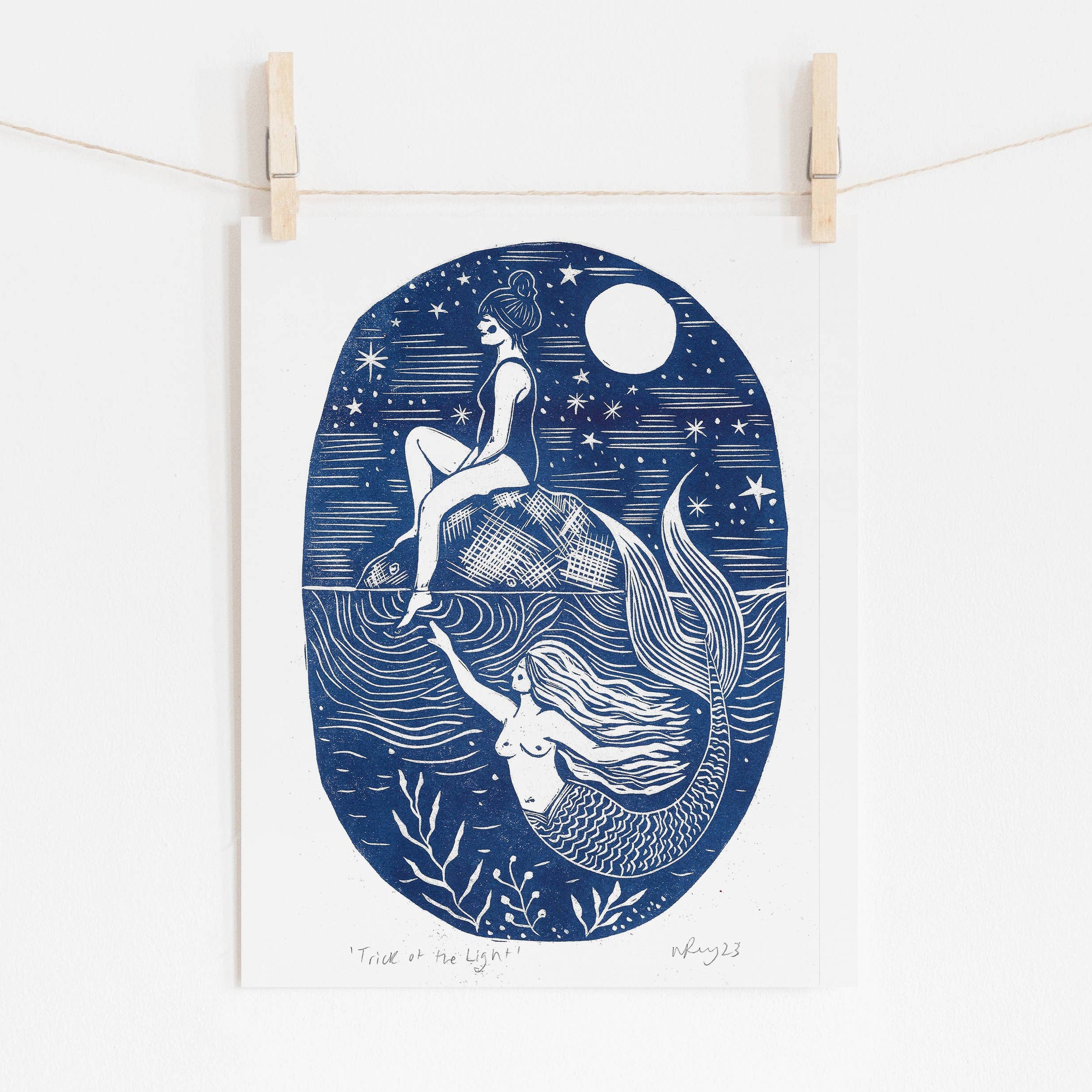 Illustration of a mermaid and a person on a blue oval background, hanging on a string with wooden clips.