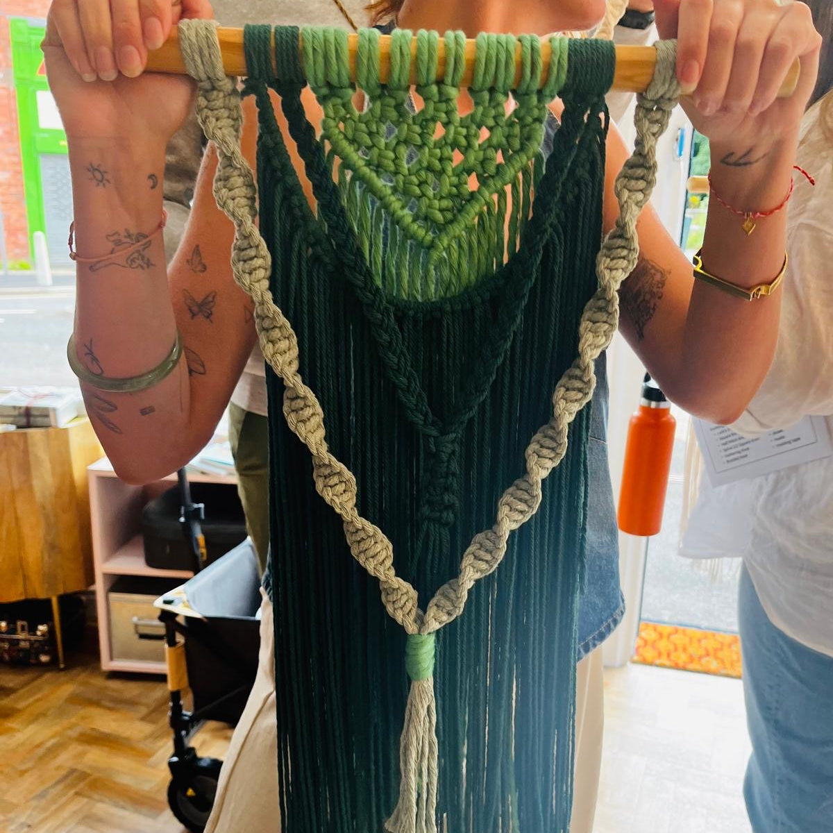 Person holding a green macramé wall hanging indoors