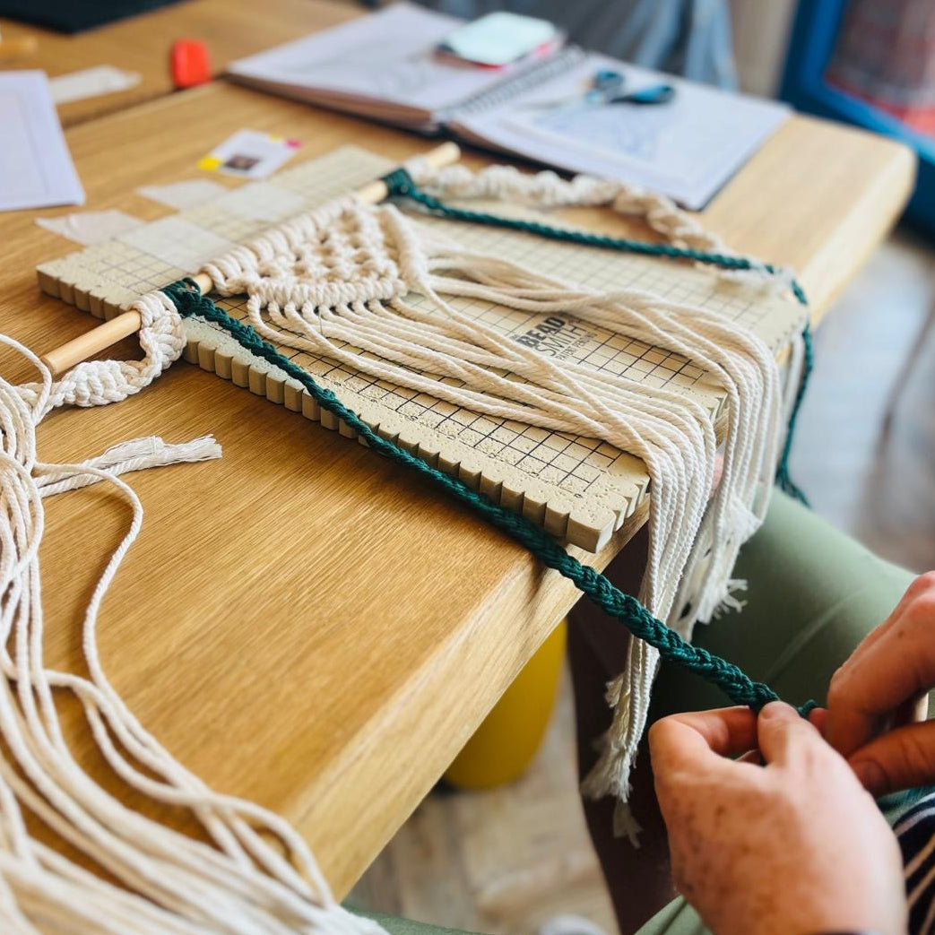 Person working on a macrame project with materials on a table.