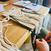 Person working on a macrame project with materials on a table.