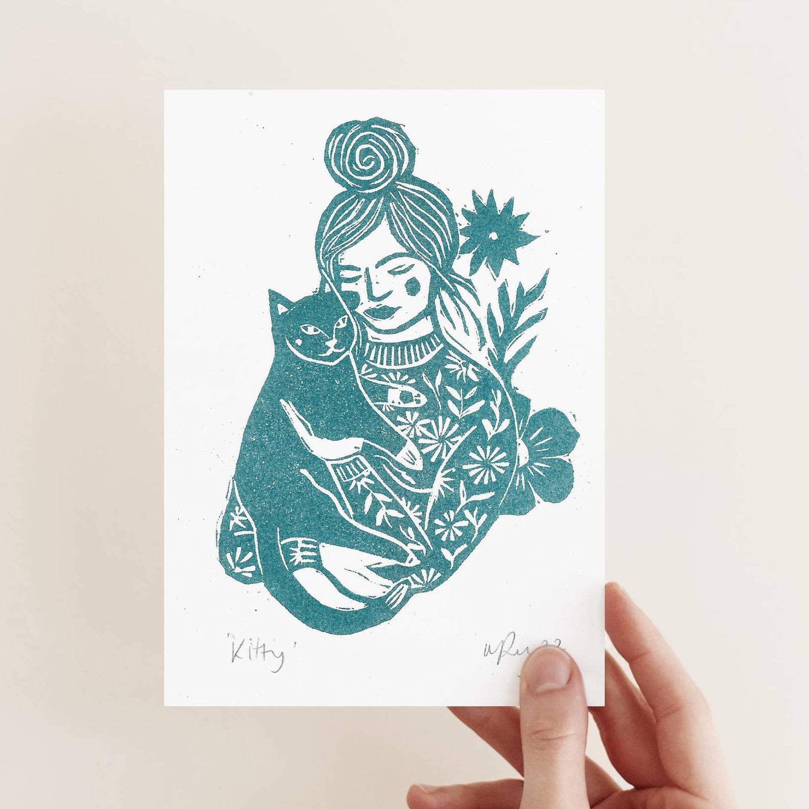 Hand holding a card with a stylized illustration of a person in a floral outfit on a beige background