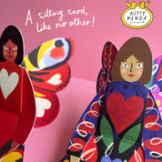 Colorful paper dolls with a butterfly and text on a pink background, featuring the Kitty Kenda brand.