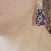 A close-up of a person's ear wearing a dangling earring made from colorful patterned fabric with a silver-toned metal top and hook.