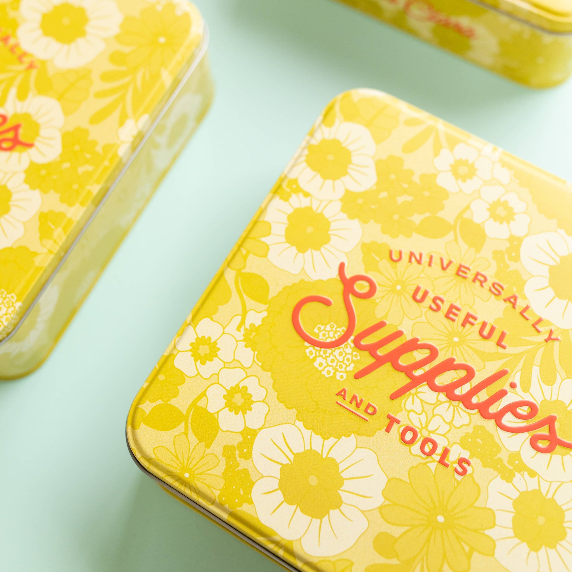 Yellow metal boxes with floral patterns and text on a light blue background