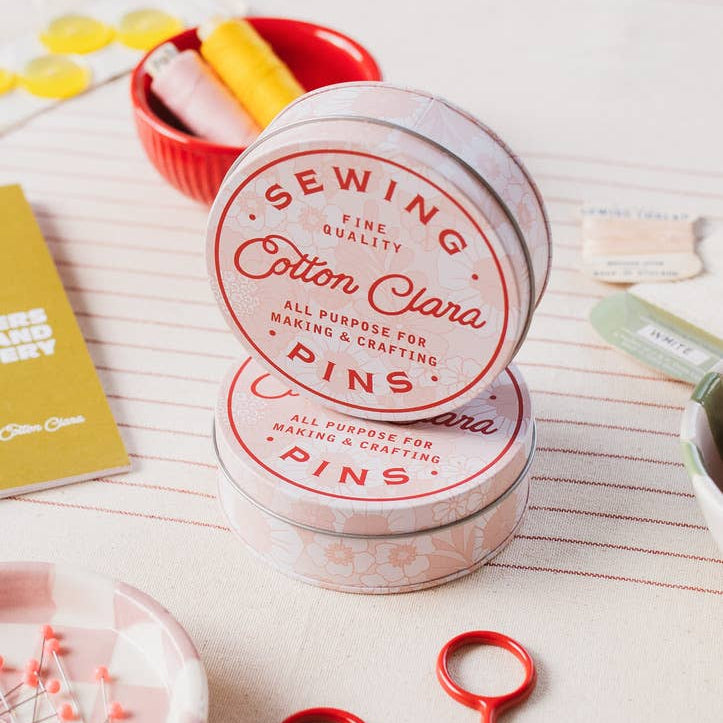 Sewing pins container with red scissors on a white surface