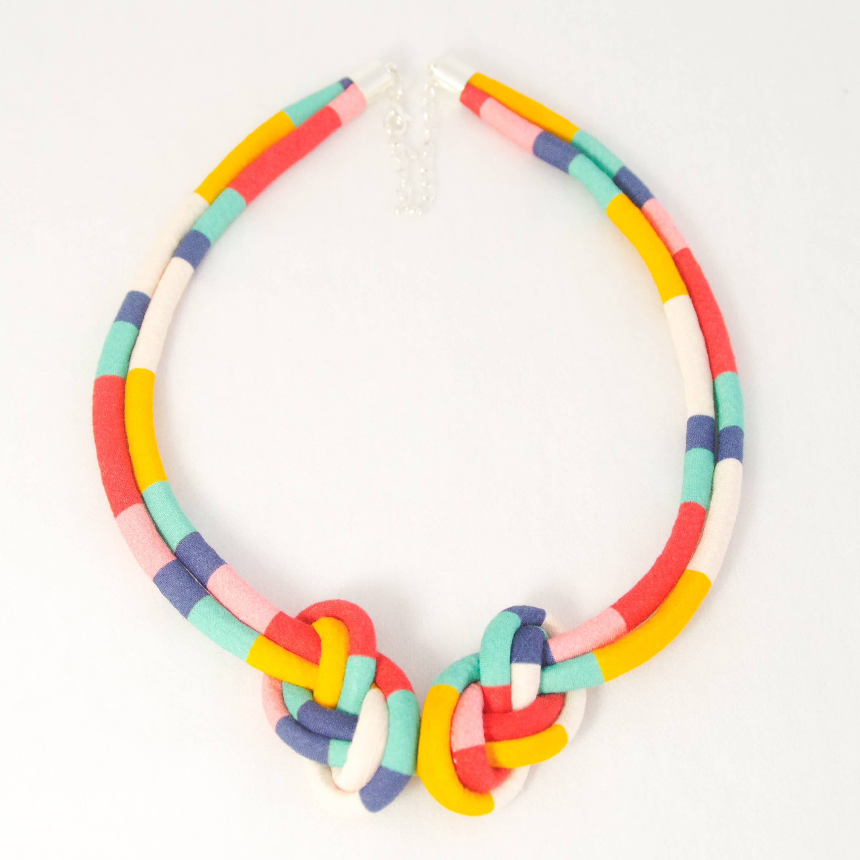 A colorful handmade polymer clay necklace with a chunky collar design, featuring a central knot with interlocking colorful clay loops. The necklace is composed of segments in yellow, red, pink, mint green, light blue, and white, photographed on a clean white background.