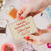 Person holding a travel sewing kit with various sewing supplies on a light surface