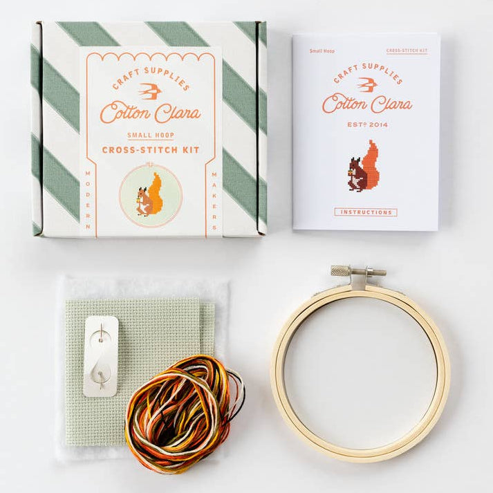 Cross-stitch kit with hoop, thread, and packaging on a white background