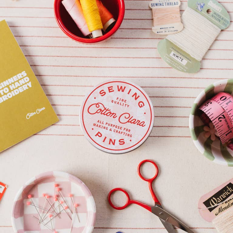 Sewing supplies including pins, thread, scissors, and a book on a wooden surface.